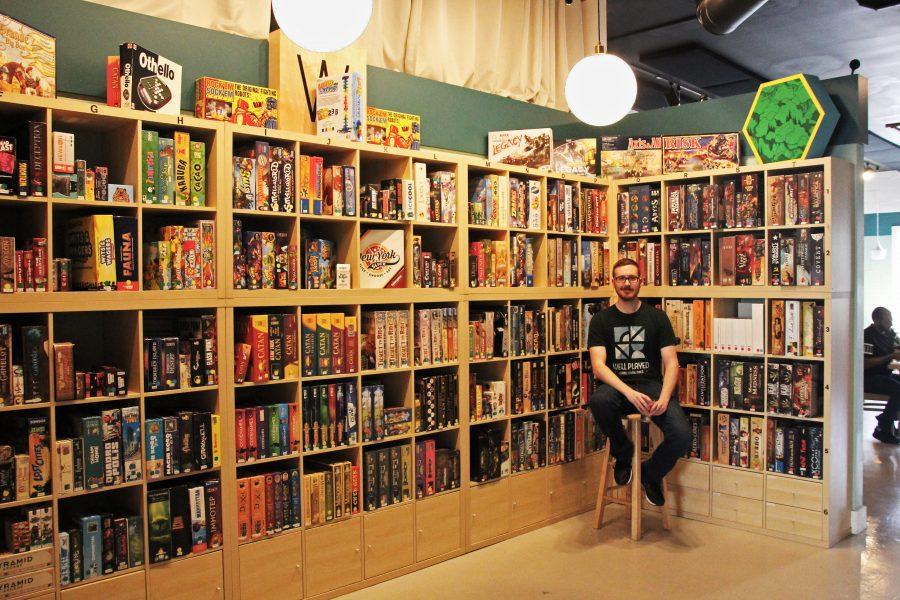 Head game master Tanner Johnson sits with the game wall, where most of the games at Well Played are kept. The business now owns over 600 games.