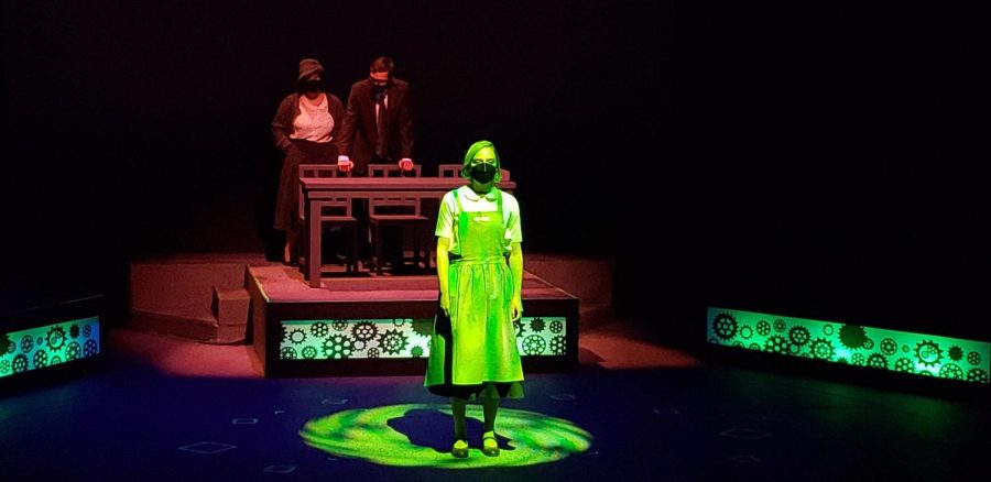 Photo courtesy of Robert Bowen: 
A student stands under a green spotlight on stage while two other
students stand in the background behind them during a performance of “Radium Girls”.