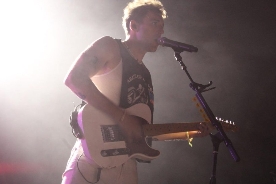 Jordan strums his guitar and sings loudly into the mic.