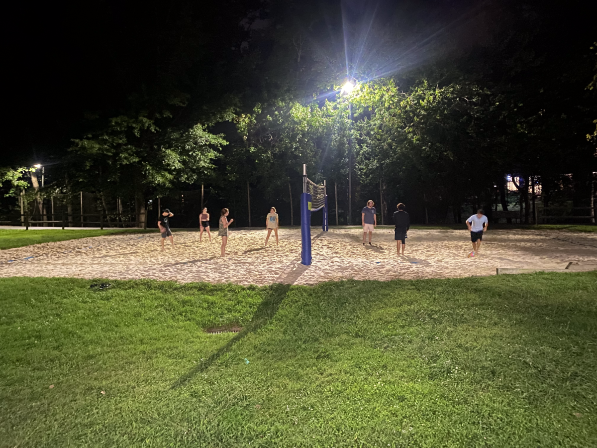 Students playing volleyball behind Mills Hall at night. 