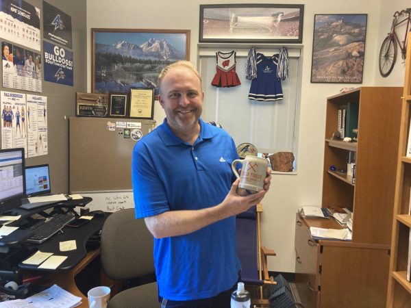 Wilcox poses in his office with a personalized mug from a former student’s business, Mica Town Brewing.