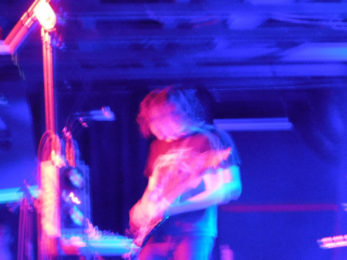 A three dimensional shot of Menashe playing their guitar.