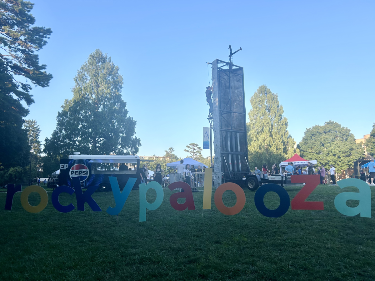 Students attempting to rock climb behind the Rockypalooza sign.